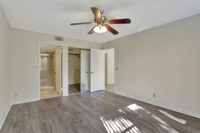 unfurnished bedroom featuring a textured ceiling, hardwood / wood-style flooring, ensuite bath, and ceiling fan