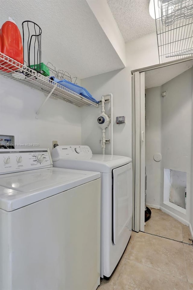 laundry area with light tile patterned flooring, washing machine and dryer, and a textured ceiling