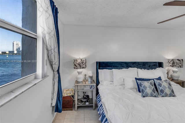 bedroom with tile patterned flooring, a textured ceiling, a water view, and ceiling fan