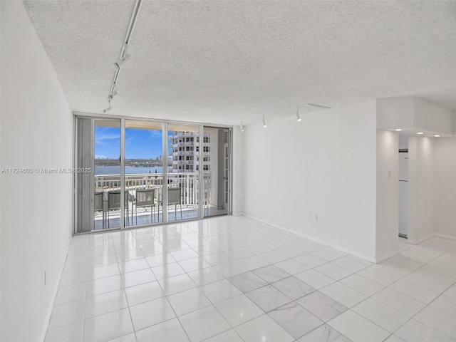 spare room with a water view, a wall of windows, a textured ceiling, and track lighting