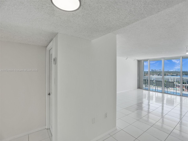 empty room with expansive windows, light tile patterned flooring, and a textured ceiling