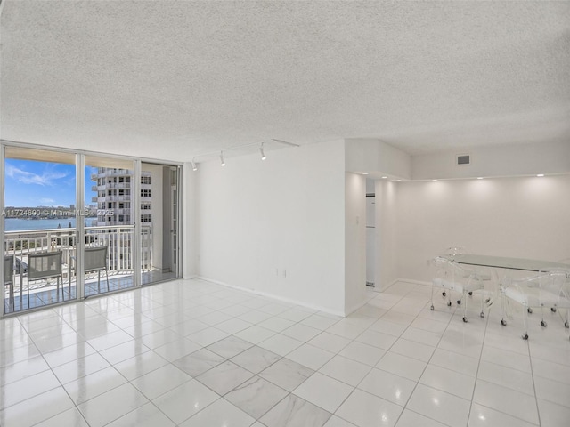 empty room with floor to ceiling windows, rail lighting, a textured ceiling, a water view, and light tile patterned floors