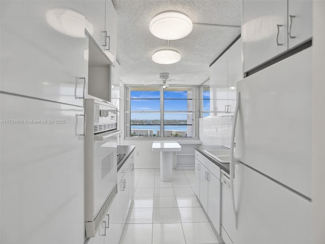 kitchen featuring light tile patterned floors, white appliances, white cabinetry, and ceiling fan