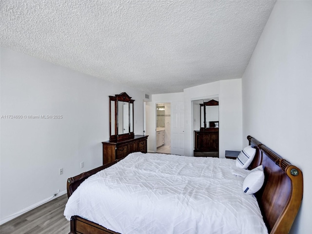 bedroom with hardwood / wood-style flooring, a textured ceiling, and connected bathroom