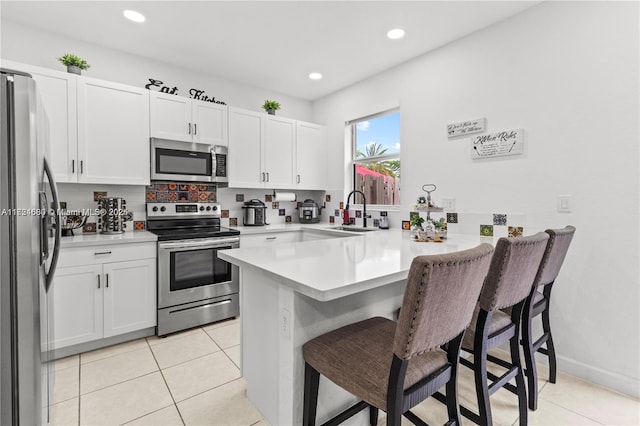 kitchen with sink, kitchen peninsula, a kitchen bar, white cabinetry, and stainless steel appliances