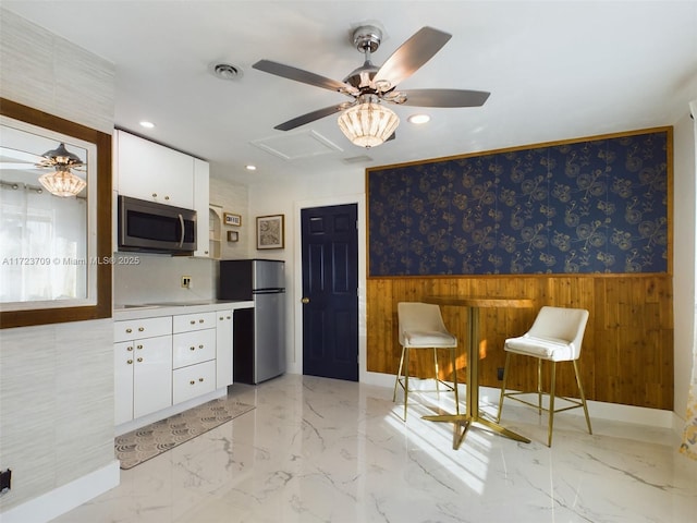 kitchen featuring stainless steel appliances, wood walls, ceiling fan, and white cabinetry