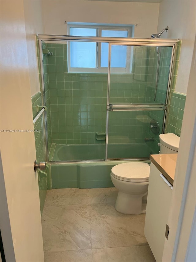 full bathroom featuring shower / bath combination with glass door, vanity, tile walls, and toilet