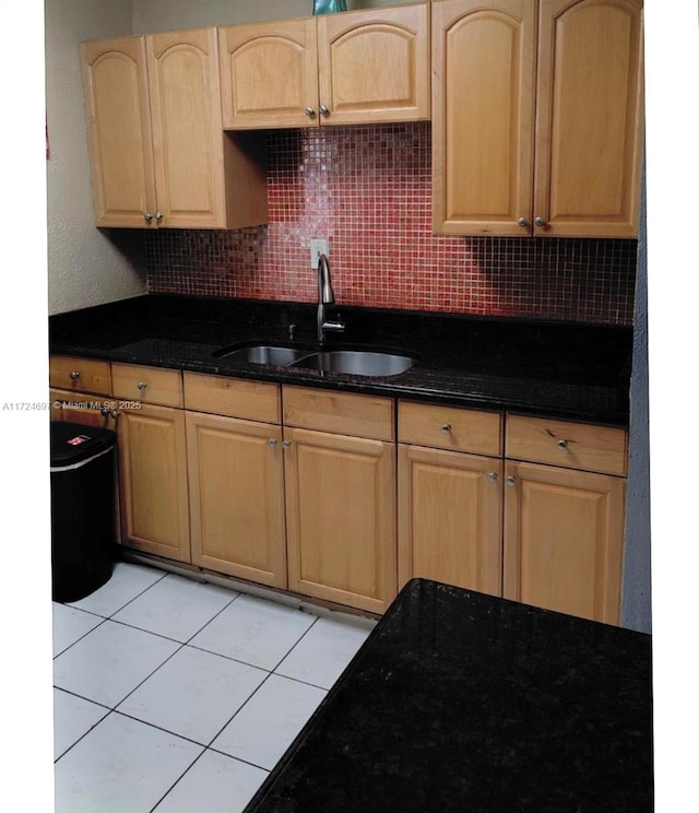 kitchen featuring light tile patterned floors, backsplash, dark stone counters, and sink