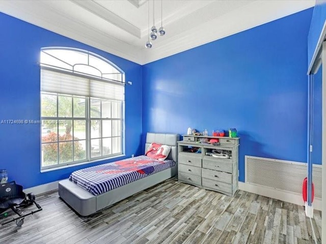 bedroom featuring ornamental molding, a tray ceiling, multiple windows, and hardwood / wood-style flooring