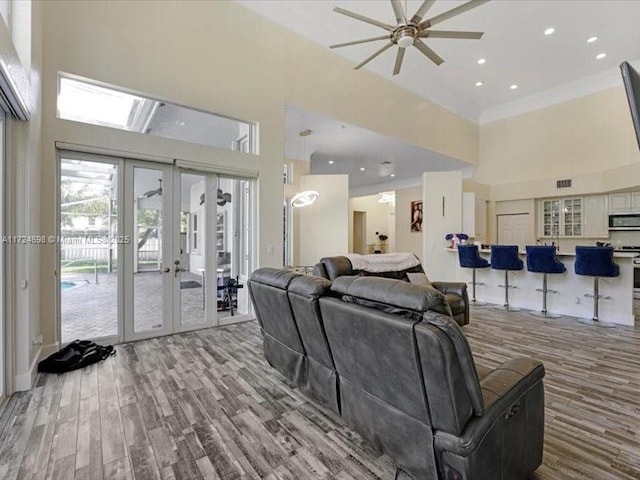 living room with light wood-type flooring, ceiling fan, ornamental molding, and french doors