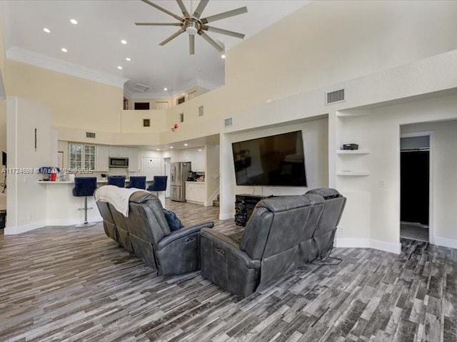 living room featuring ceiling fan, wood-type flooring, a towering ceiling, and ornamental molding