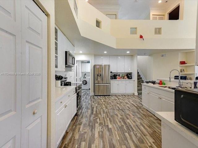 kitchen featuring a towering ceiling, washer / clothes dryer, white cabinetry, stainless steel appliances, and sink