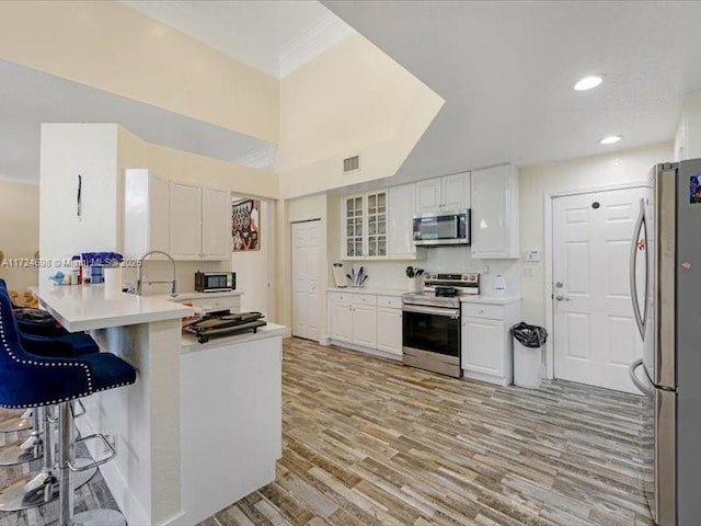 kitchen with kitchen peninsula, white cabinets, a kitchen bar, and stainless steel appliances