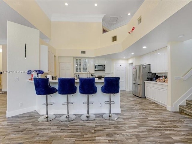 kitchen featuring white cabinets, appliances with stainless steel finishes, kitchen peninsula, crown molding, and a breakfast bar area