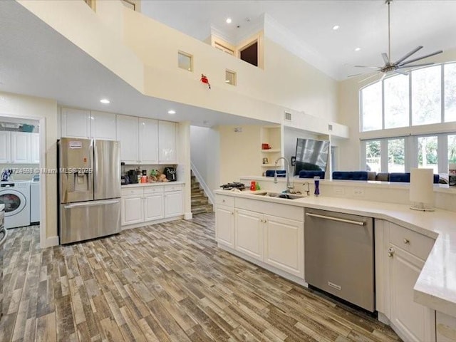 kitchen featuring appliances with stainless steel finishes, washer and dryer, a high ceiling, white cabinets, and sink