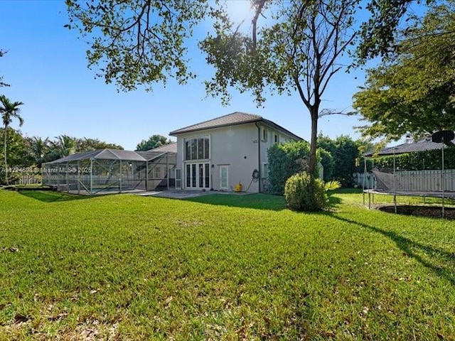 rear view of property with glass enclosure, a lawn, french doors, and a trampoline