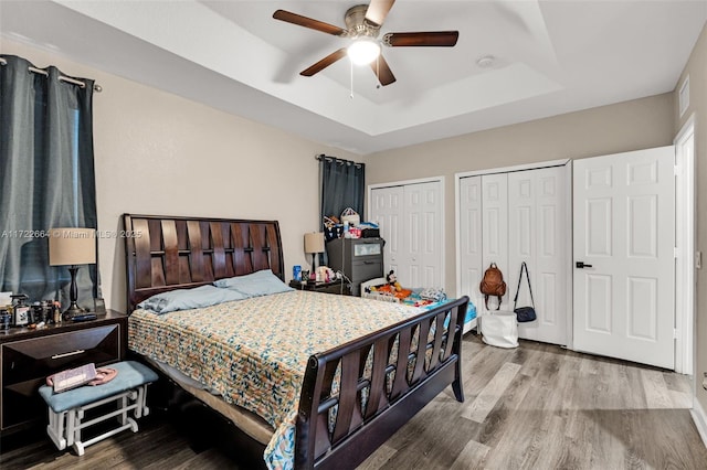 bedroom with a tray ceiling, ceiling fan, hardwood / wood-style floors, and two closets