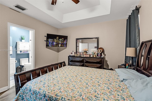 bedroom featuring a tray ceiling, ensuite bath, ceiling fan, and hardwood / wood-style flooring