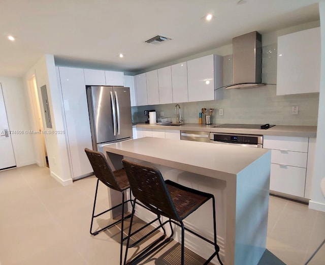 kitchen with a center island, white cabinetry, wall chimney range hood, and appliances with stainless steel finishes