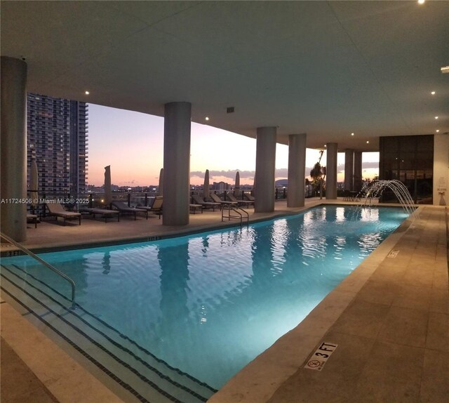 pool at dusk with a patio area and pool water feature