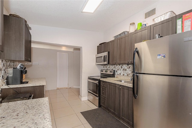 kitchen with light tile patterned floors, a textured ceiling, tasteful backsplash, dark brown cabinets, and stainless steel appliances