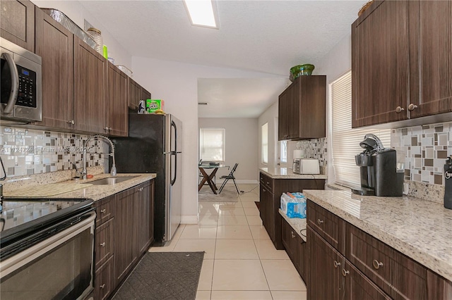 kitchen with sink, light tile patterned floors, appliances with stainless steel finishes, dark brown cabinets, and light stone counters