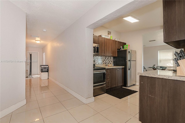 kitchen with backsplash, light tile patterned floors, a textured ceiling, and appliances with stainless steel finishes