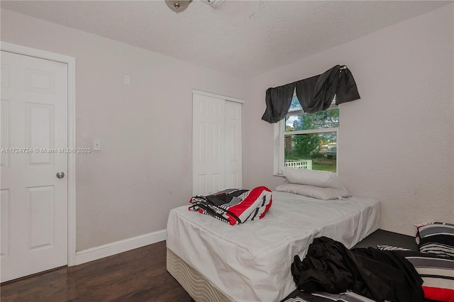 bedroom with a textured ceiling, dark wood-type flooring, and a closet