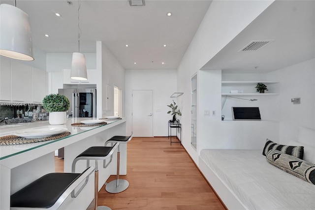 kitchen featuring white cabinetry, hanging light fixtures, stainless steel fridge, a kitchen bar, and light wood-type flooring