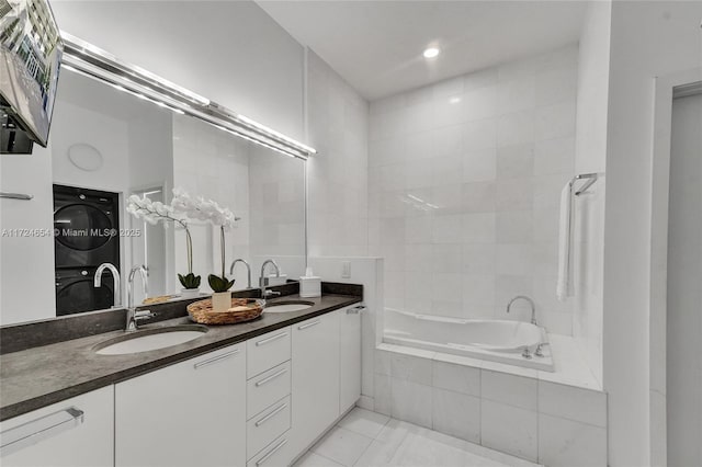 bathroom featuring tiled tub, stacked washer and dryer, vanity, and tile patterned flooring