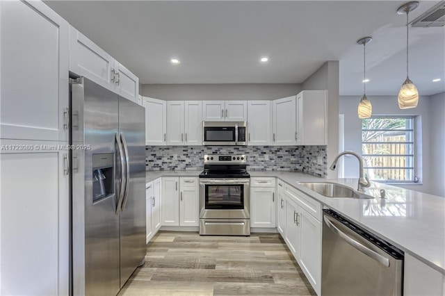 kitchen featuring pendant lighting, decorative backsplash, sink, white cabinetry, and appliances with stainless steel finishes