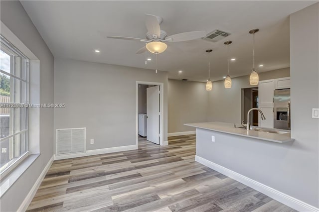 kitchen featuring stainless steel fridge, ceiling fan, hanging light fixtures, white cabinets, and sink