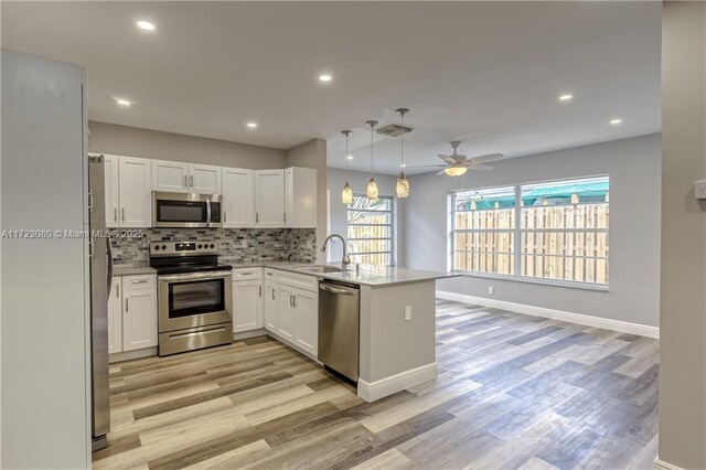 kitchen with kitchen peninsula, stainless steel appliances, decorative light fixtures, white cabinets, and sink