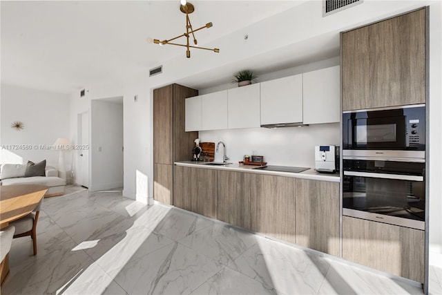 kitchen with built in microwave, white cabinetry, stainless steel oven, sink, and decorative light fixtures