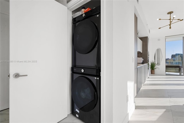 clothes washing area featuring an inviting chandelier and stacked washer and clothes dryer