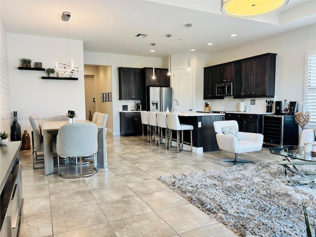 kitchen with pendant lighting, stainless steel appliances, dark brown cabinets, and a center island with sink