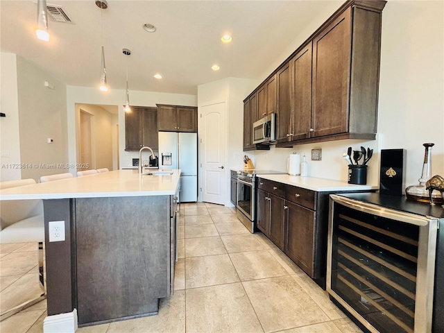 kitchen with dark brown cabinets, stainless steel appliances, a center island with sink, wine cooler, and hanging light fixtures