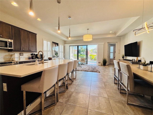 kitchen featuring appliances with stainless steel finishes, dark brown cabinetry, a tray ceiling, sink, and decorative light fixtures