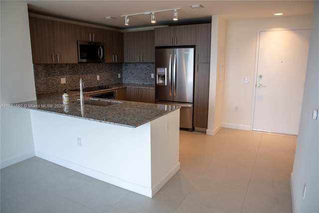 kitchen with dark stone counters, sink, appliances with stainless steel finishes, dark brown cabinets, and kitchen peninsula