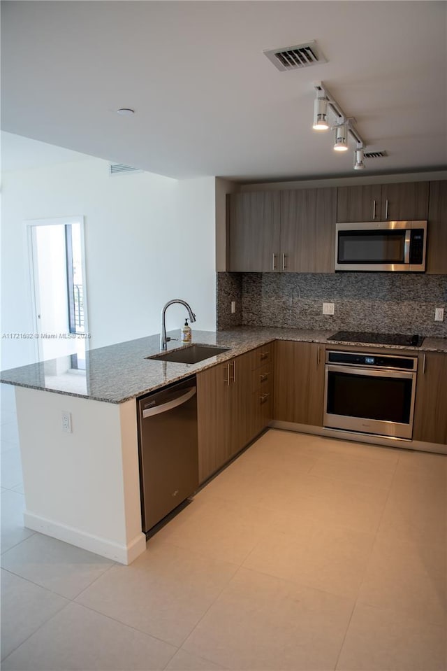 kitchen with tasteful backsplash, stainless steel appliances, sink, stone counters, and light tile patterned flooring