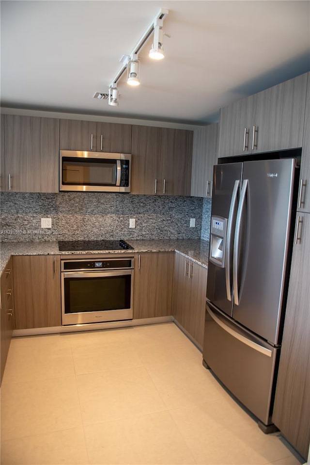 kitchen with rail lighting, dark stone countertops, appliances with stainless steel finishes, tasteful backsplash, and light tile patterned flooring