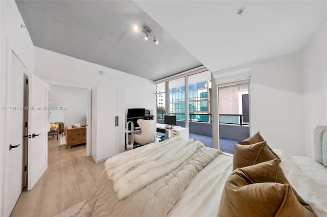 bedroom featuring rail lighting, access to exterior, floor to ceiling windows, and light hardwood / wood-style flooring