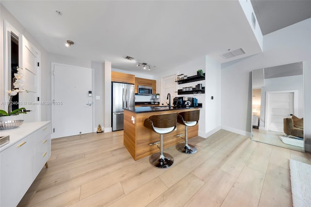 kitchen featuring a kitchen island, a breakfast bar, white cabinetry, light wood-type flooring, and appliances with stainless steel finishes