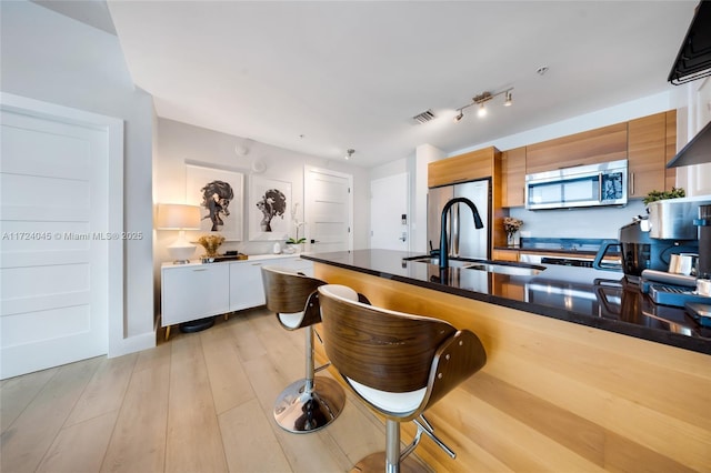 kitchen featuring light wood-type flooring, a breakfast bar area, white cabinets, appliances with stainless steel finishes, and sink