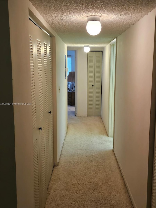 hallway featuring light colored carpet and a textured ceiling