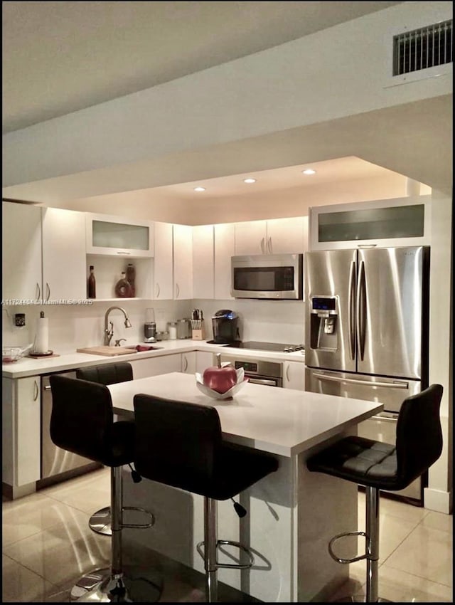 kitchen with white cabinets, sink, light tile patterned floors, a kitchen bar, and stainless steel appliances