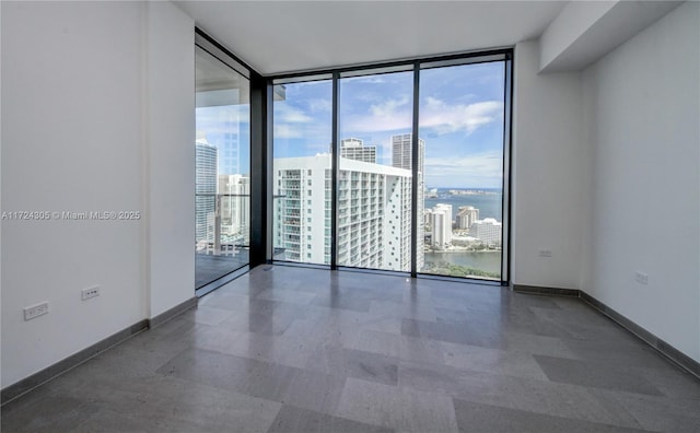 unfurnished room featuring a city view, a wall of windows, and baseboards