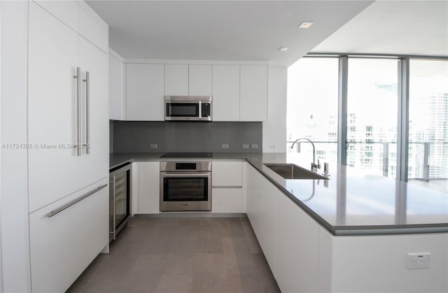 kitchen with a sink, appliances with stainless steel finishes, a peninsula, white cabinetry, and modern cabinets