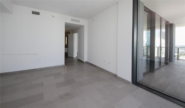 spare room with a wall of windows, visible vents, baseboards, and light floors