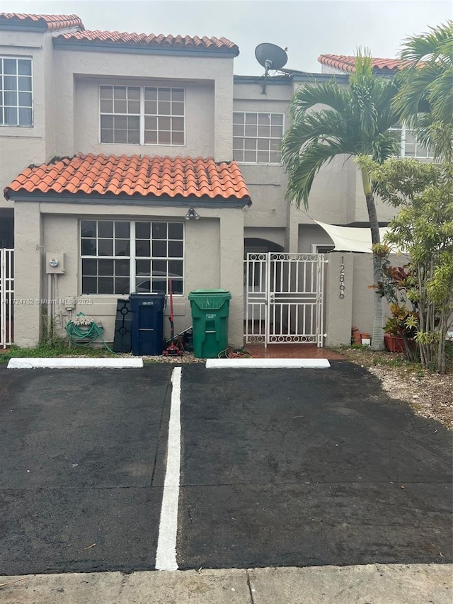 back of property with a tiled roof, uncovered parking, a gate, and stucco siding